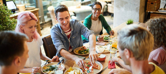Happy group of friends enjoying a meal at a restaurant, symbolizing comfortable digestion and less bloating with enzyme support